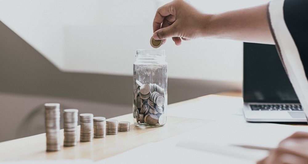 Fotografía en el blog de Chapa Cambio sobre cómo ahorrar e invertir, mostrando a una persona depositando monedas en un frasco, representando la importancia del ahorro y la inversión para el crecimiento financiero