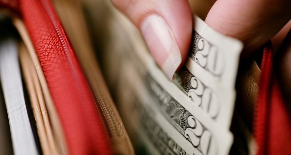 Imagen de una entrada del blog de Chapa Cambio sobre cómo gastar menos dinero, mostrando una mano sacando dólares de una billetera, simbolizando la importancia de la gestión eficiente del dinero y los consejos prácticos para ahorrar más