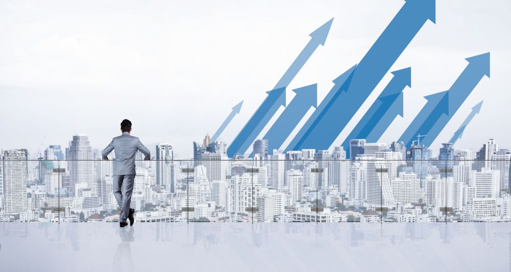 Imagen de una entrada del blog de Chapa Cambio sobre inversiones alternativas, mostrando a un empresario observando la ciudad con flechas azules ascendentes, simbolizando el crecimiento y las oportunidades en el mercado financiero