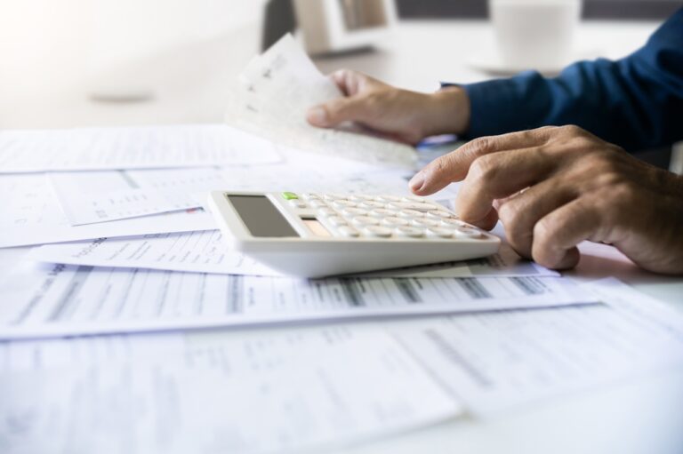 Imagen de una persona usando una calculadora y revisando facturas, utilizada en una entrada en el blog de Chapa Cambio sobre la producción de ingresos en el extranjero y obligaciones fiscales